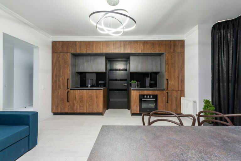Creative design of kitchen with cupboards and built in oven against table and sofa in house with geometric lamp